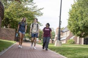 Three students walking across campus with Grace Chapel and Shaw Plaza in the background